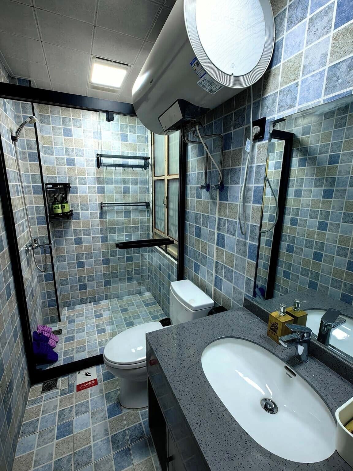 A bathroom with a shower, toilet, and sink, tiled in blue and gray.