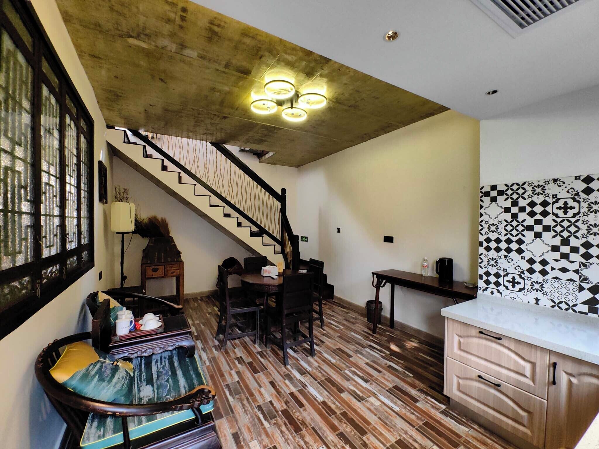 Uma escadaria que dá acesso a um segundo andar, uma área de jantar com mesa e cadeiras, uma cozinha com painel de fundo estampado e piso de madeira.
