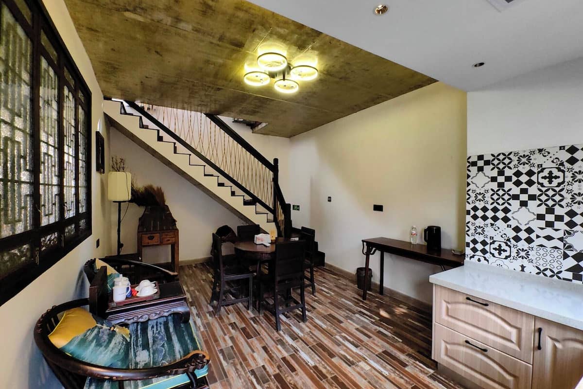 A staircase leading to a second floor, a dining area with a table and chairs, a kitchen with a patterned backsplash, and a wooden floor.