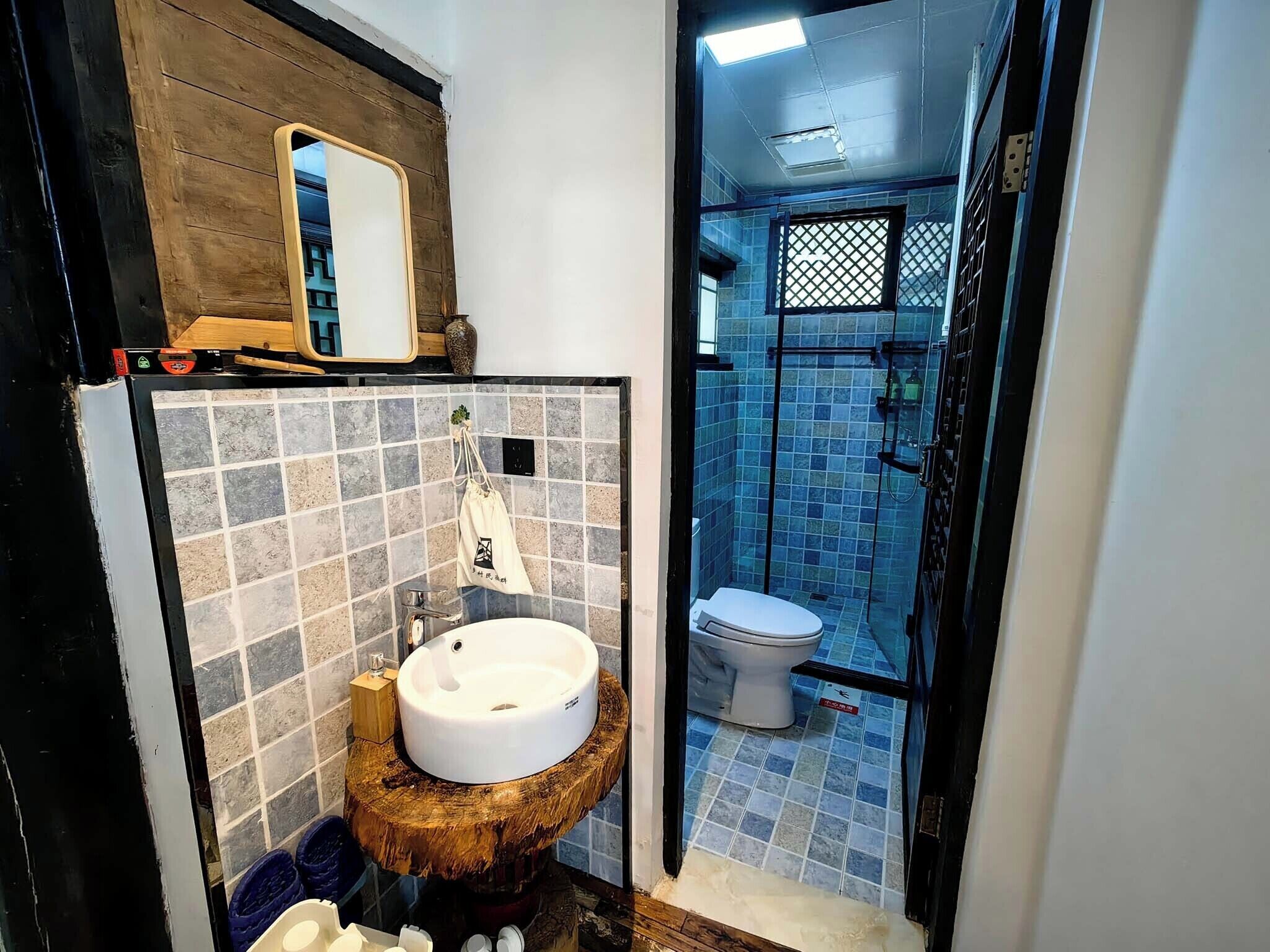 Casa de banho com toucador de madeira, lavatório, espelho e zona de duche com azulejos azuis.