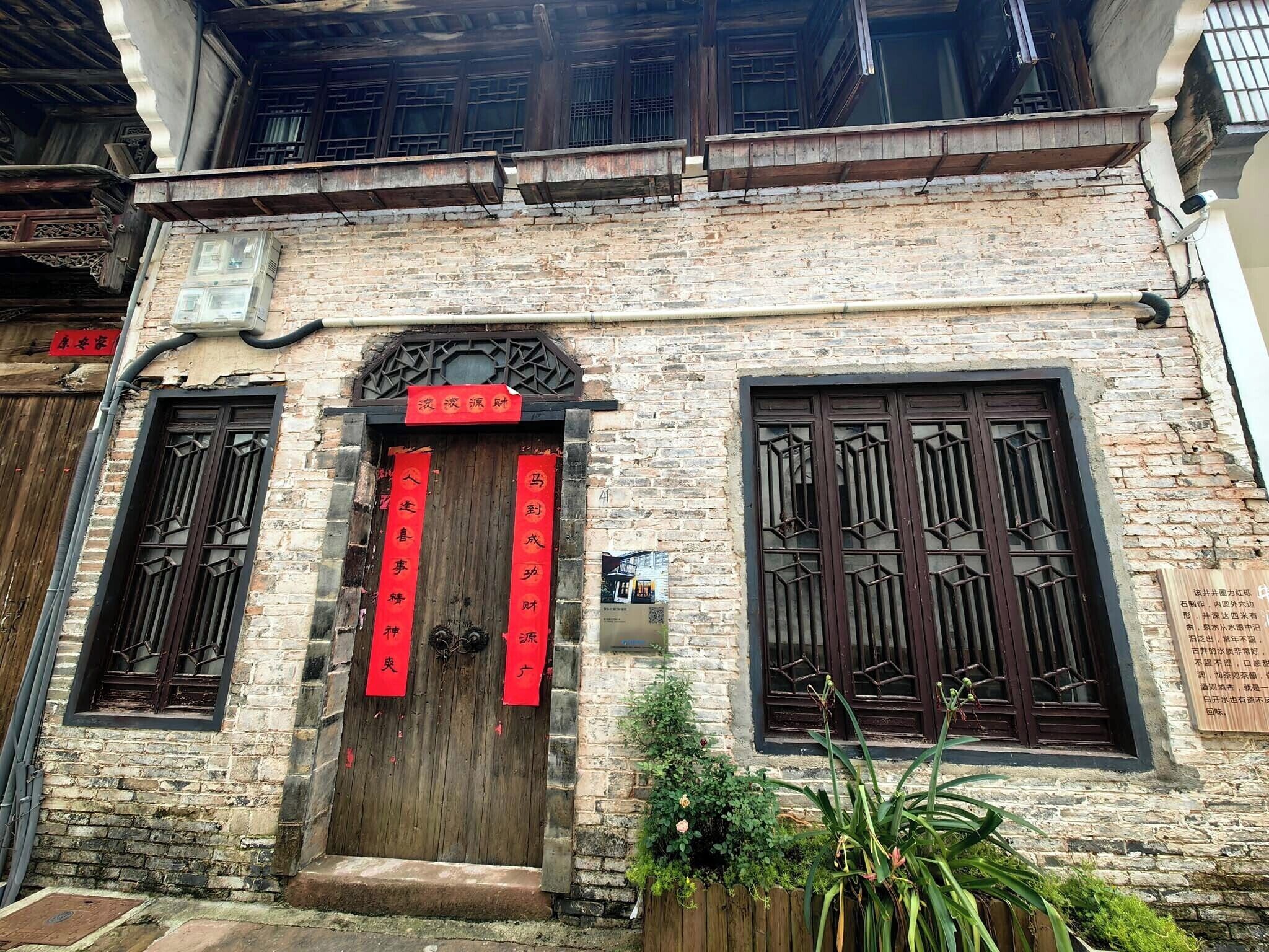 A traditional building with a wooden door, two windows with decorative grills, and a brick facade.