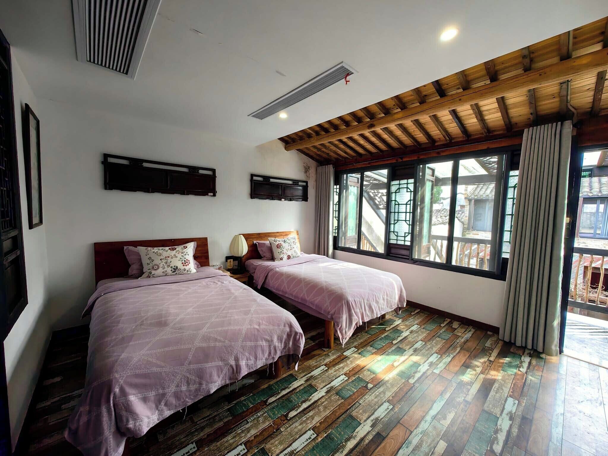 Quarto com duas camas, piso de madeira, teto inclinado e janela com vista para escadas externas.