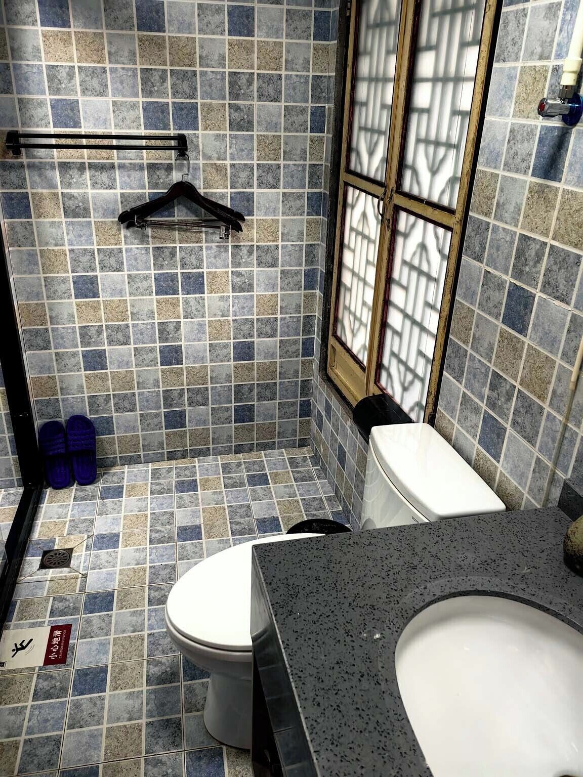 A bathroom with a tiled floor, a toilet, a sink, and a window.