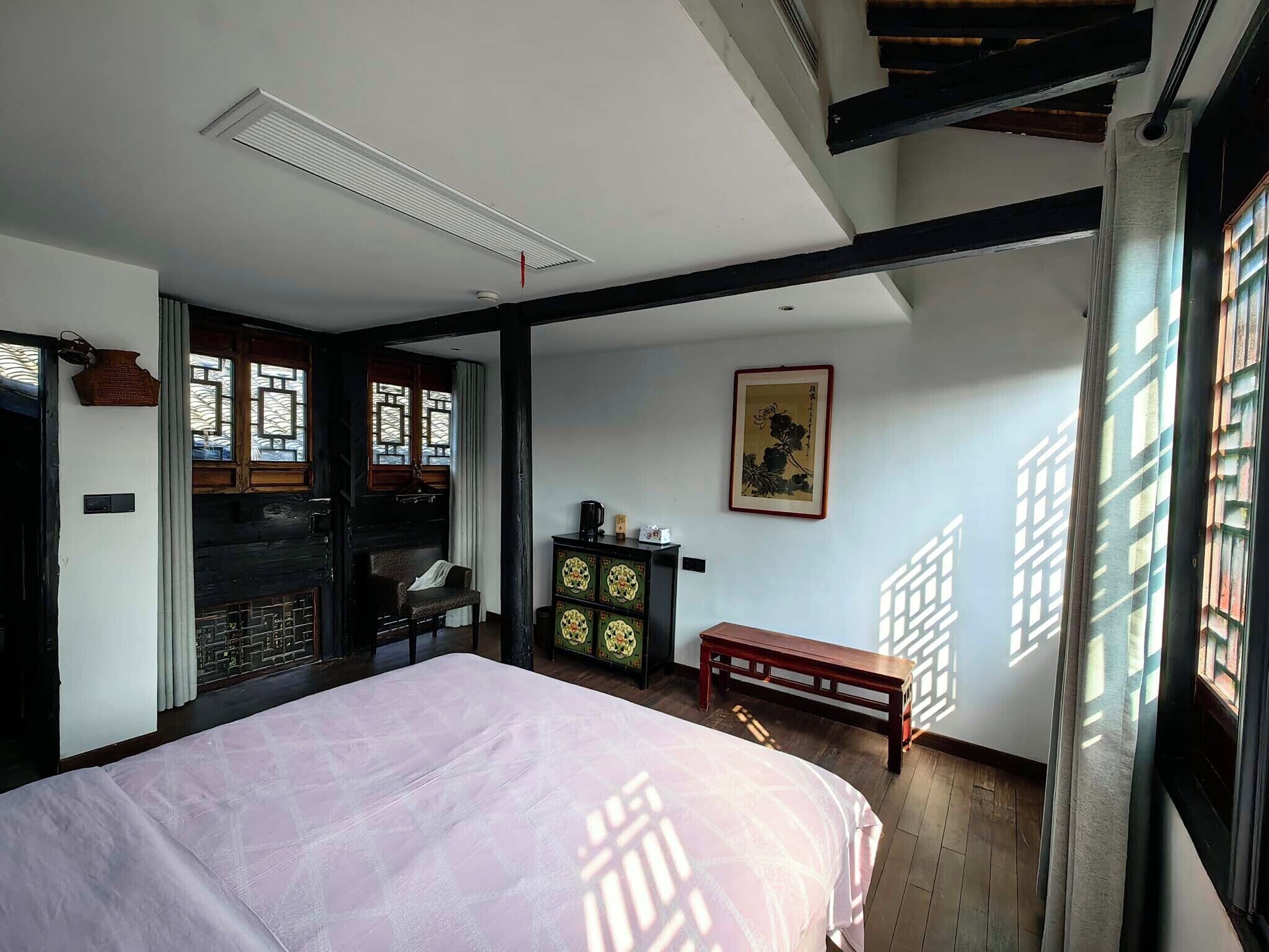 Quarto com cama, um banquinho de madeira, um armário e um quadro tradicional na parede.