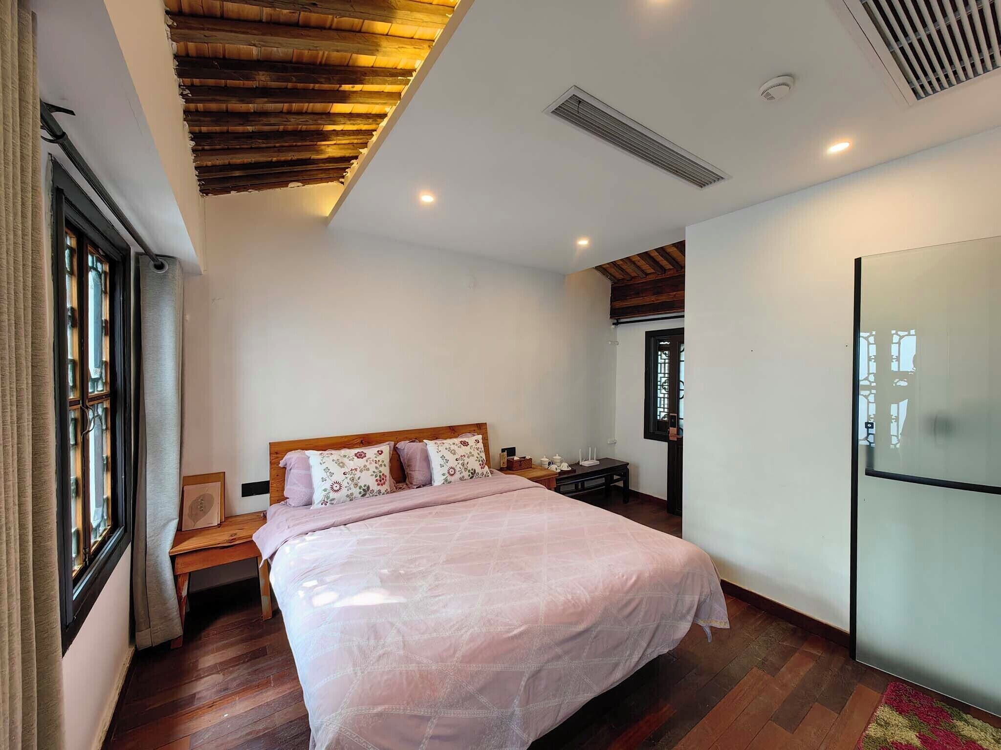 Quarto com teto de madeira, cama com colcha florida, mesa de cabeceira e janela com cortinas.