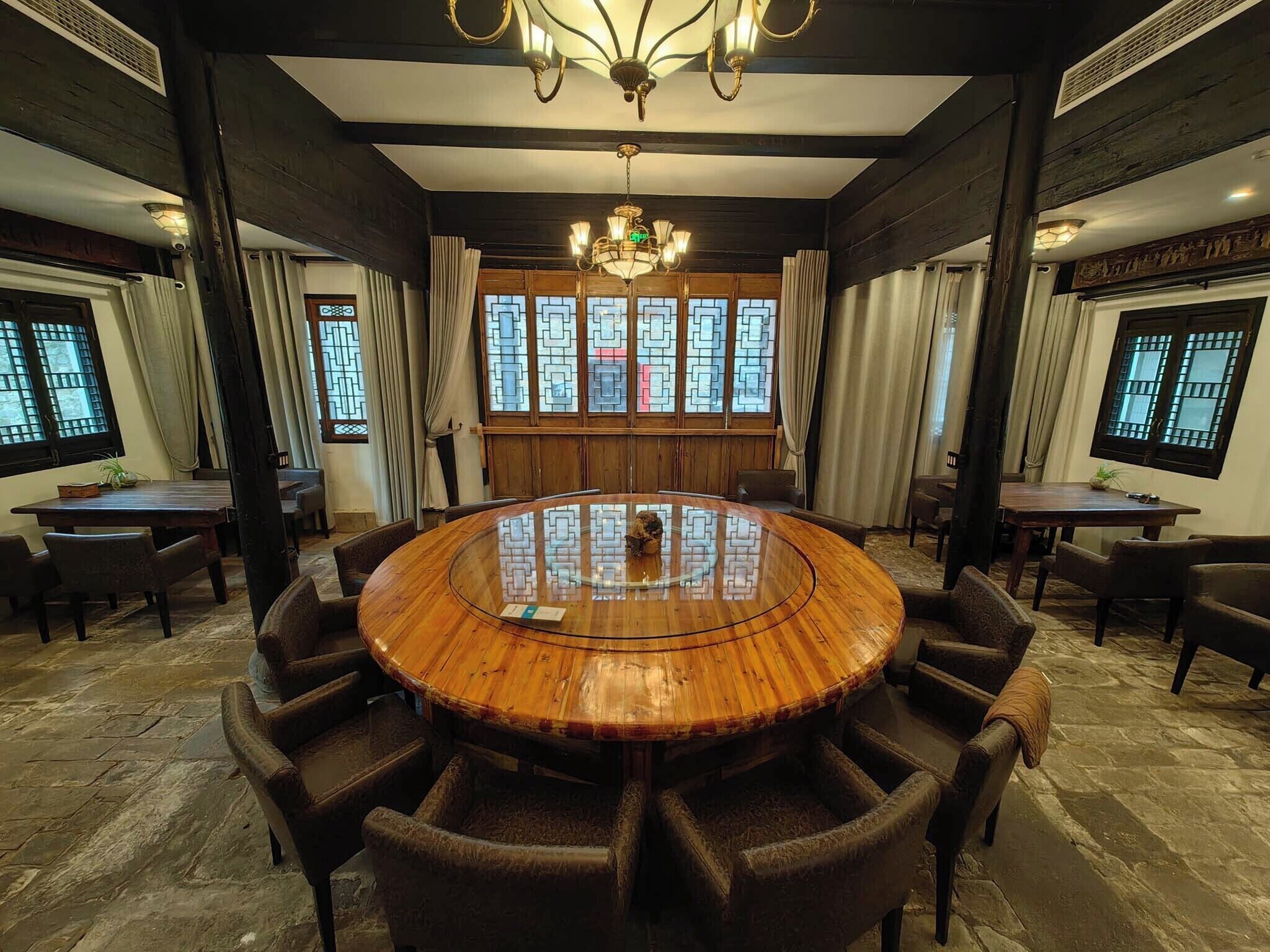 A conference room with a round wooden table, dark wooden chairs, a chandelier, and large windows with traditional lattice designs.
