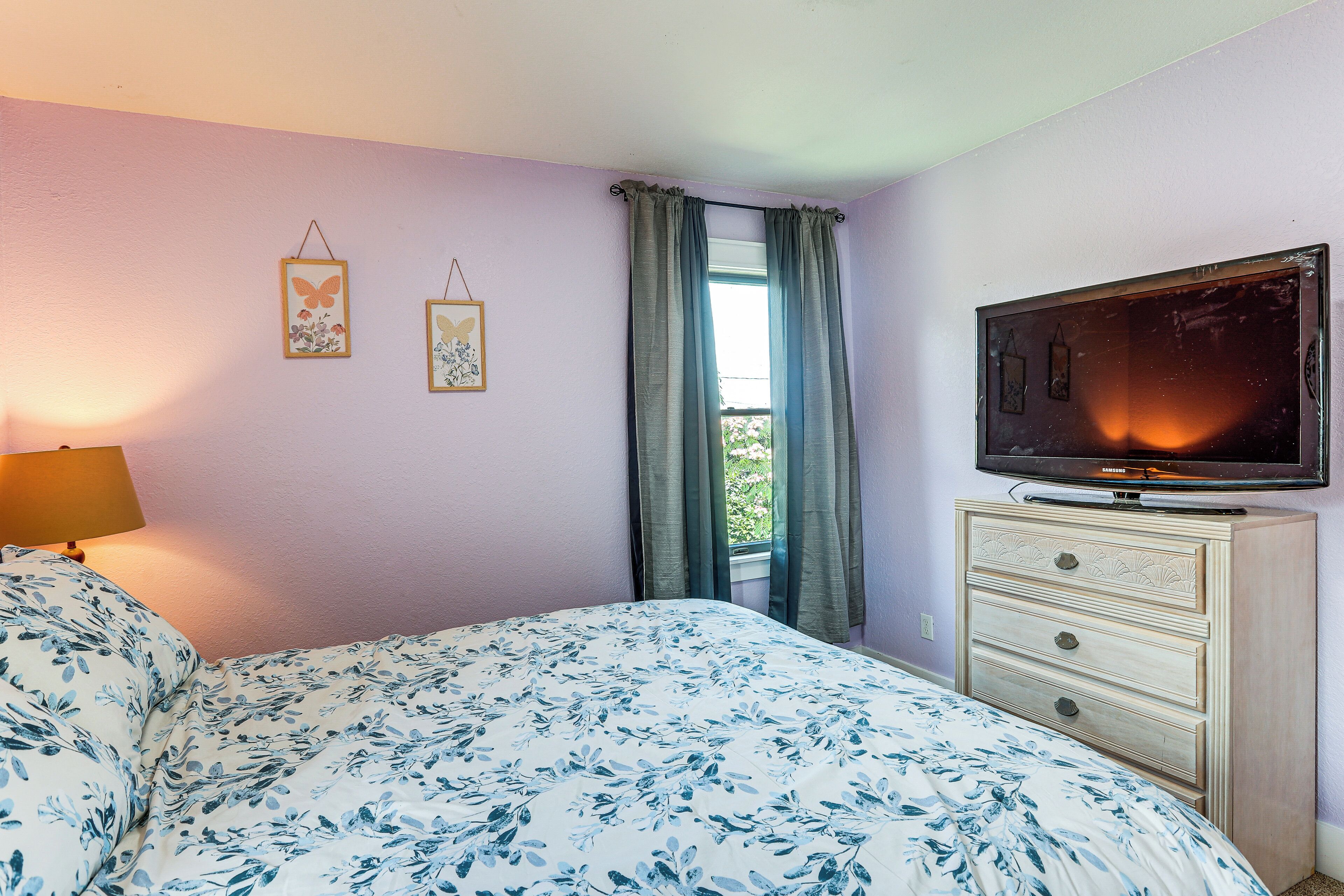 Une chambre à coucher comprenant un lit, une commode, un téléviseur et deux tableaux accrochés au mur.