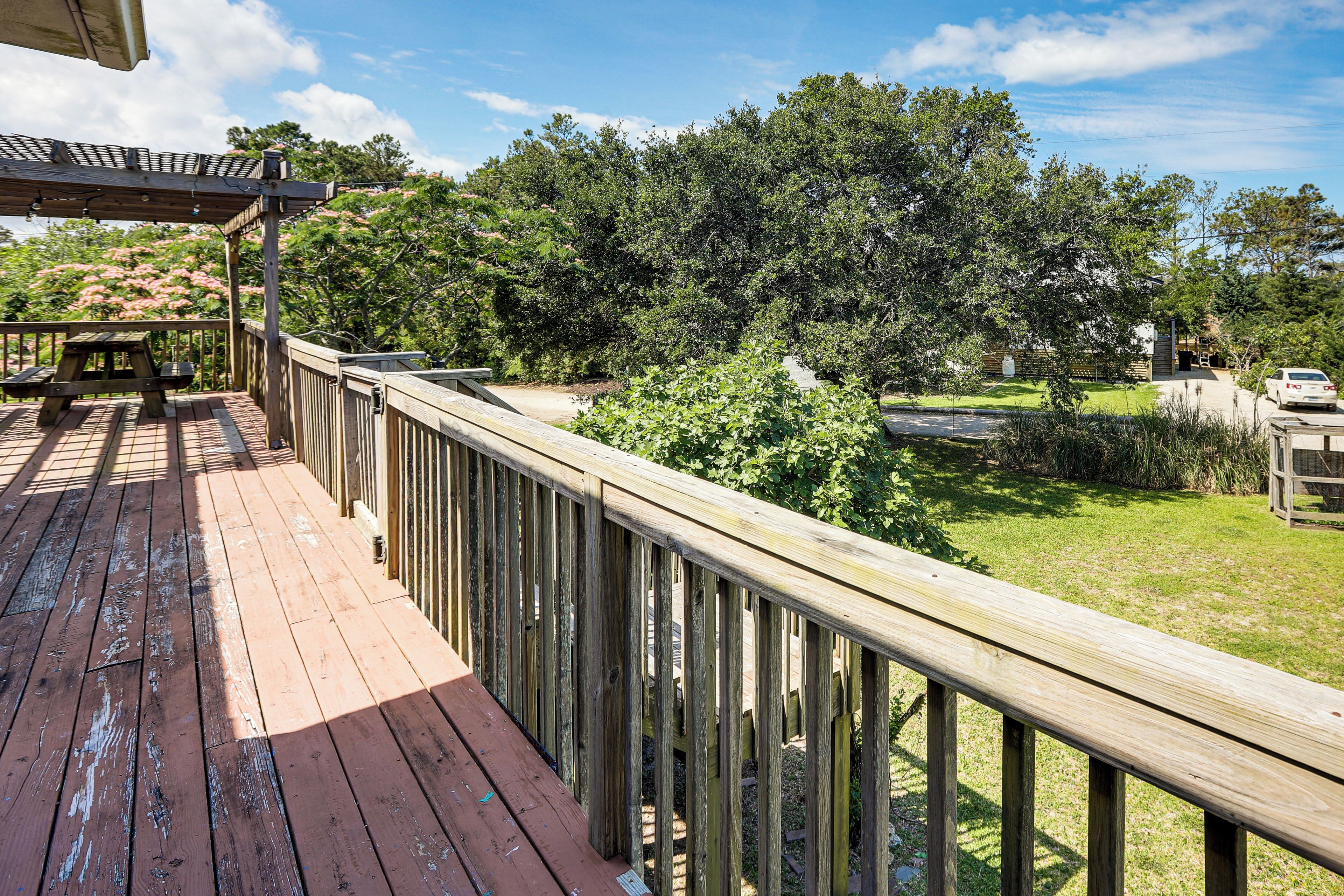 A wooden deck with a picnic table, surrounded by lush greenery and trees.