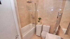 A bathroom with a glass-enclosed shower, a toilet, a sink, and a small potted plant.