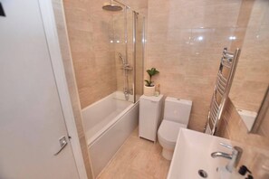 A bathroom with a glass-enclosed shower, a toilet, a sink, and a small potted plant. - Studio flat in heart of Balham (Greater London)