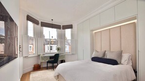 A bedroom with a bed, a desk, and a view of the city.