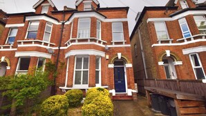 A row of red brick terraced houses with bay windows, white trim, and a blue door.