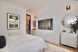 A bedroom with a bed, a framed book, a painting, a mirror, and a cabinet. - Studio flat in heart of Balham (Greater London)