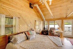A wooden cabin bedroom with a bed, a chair, a table, and a fireplace. - Waterfront Berkshires Studio w/ Dock on Goose Pond (Lee)