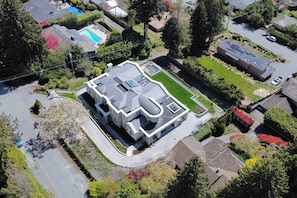 An aerial view of a modern house with a unique curved roof, surrounded by a well-maintained garden and a swimming pool. - West Van Luxury Retreat 2BR 2BA Oceanview (West Vancouver)