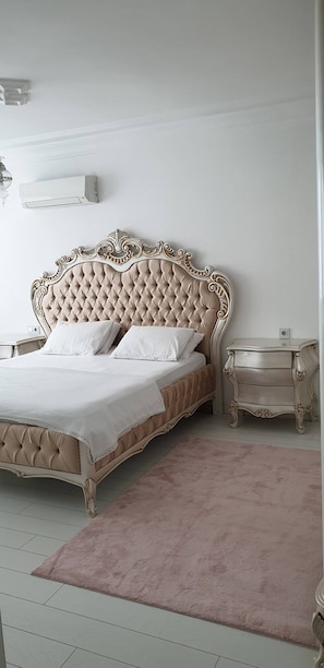 A bedroom with a tufted headboard, a bedside table, a nightstand, a pink rug, and an air conditioning unit on the wall. - King's apartment 10 min to Konyaalti beach (Muratpaşa)