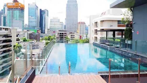 Ein Schwimmbad mit Blick auf die Stadt, moderne Gebäude und ein Baukran im Hintergrund.
