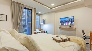 Ein Hotelzimmer mit einem großen Bett, einem Fernseher, einem Schreibtisch mit Stuhl und Blick ins Freie.