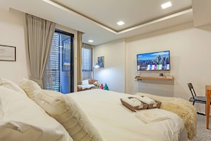 Ein Hotelzimmer mit einem großen Bett, einem Fernseher, einem Schreibtisch mit Stuhl und Blick ins Freie.