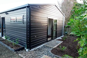 Ein modernes, eingeschossiges Gebäude mit Metallfassade, einer Schiebetür aus Glas und einem kleinen Gartenbereich mit Kies und Pflanzen.