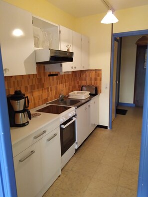Uma cozinha compacta com armários brancos, fogão, pia e torradeira.