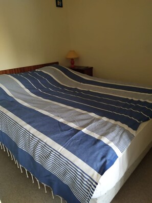 Uma cama com colcha listrada, uma mesa de cabeceira com abajur e um quadro na parede.