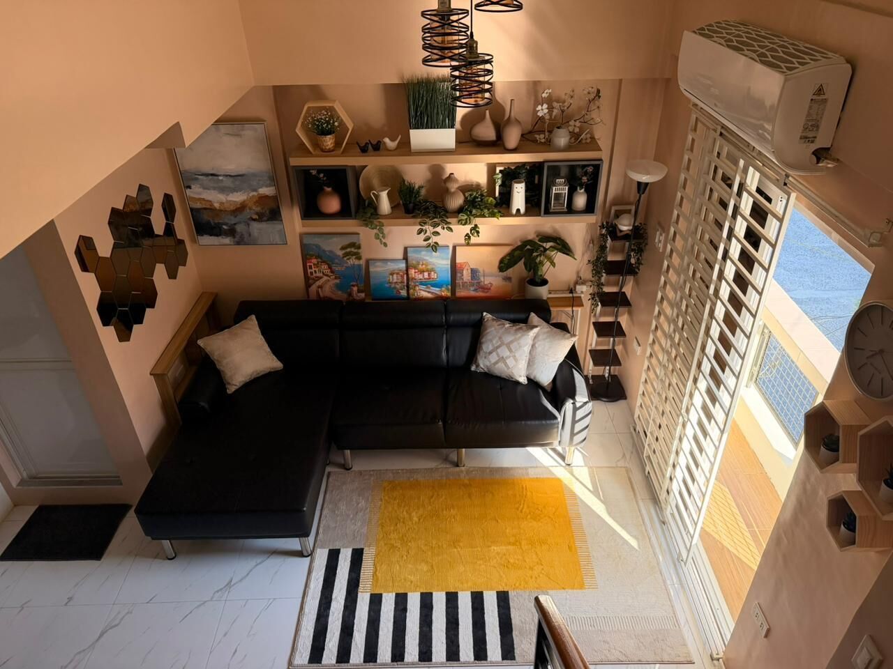 Ein modernes Wohnzimmer mit einem schwarzen Sofa, einem gelben Teppich und verschiedenen Dekoartikeln auf Regalen.