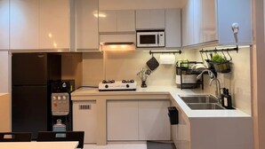 Een moderne keuken met witte kastjes, een zwarte koelkast, een magnetron, een gasfornuis, een waterdispenser en een spoelbak.