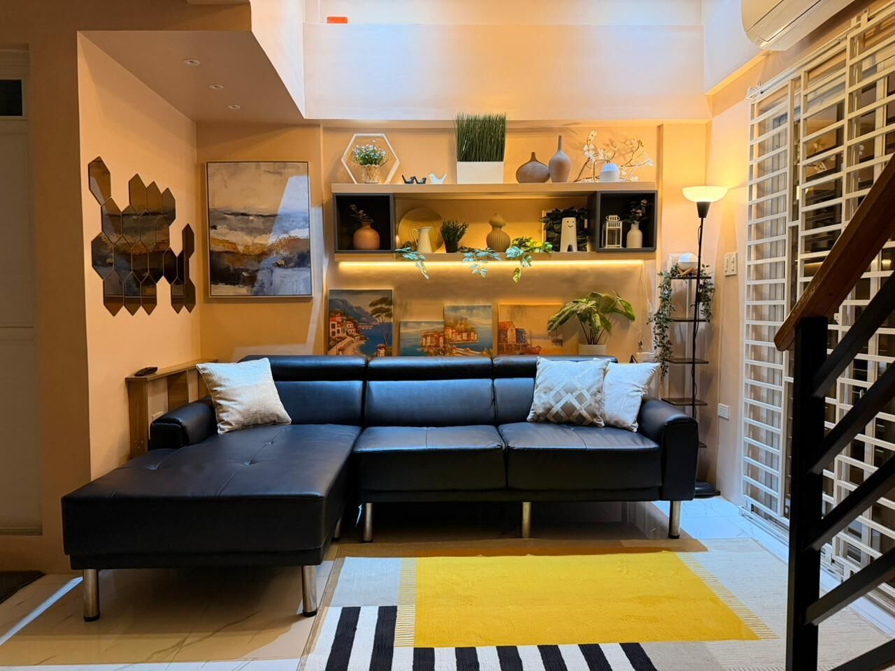 A modern living room with a sectional sofa, a yellow rug, and decorative shelves.. Welcoming 1-bedroom apartment with AC in charming Lucban