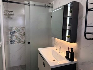 A bathroom with a shower, a sink, a mirror, and a shelf with plants.