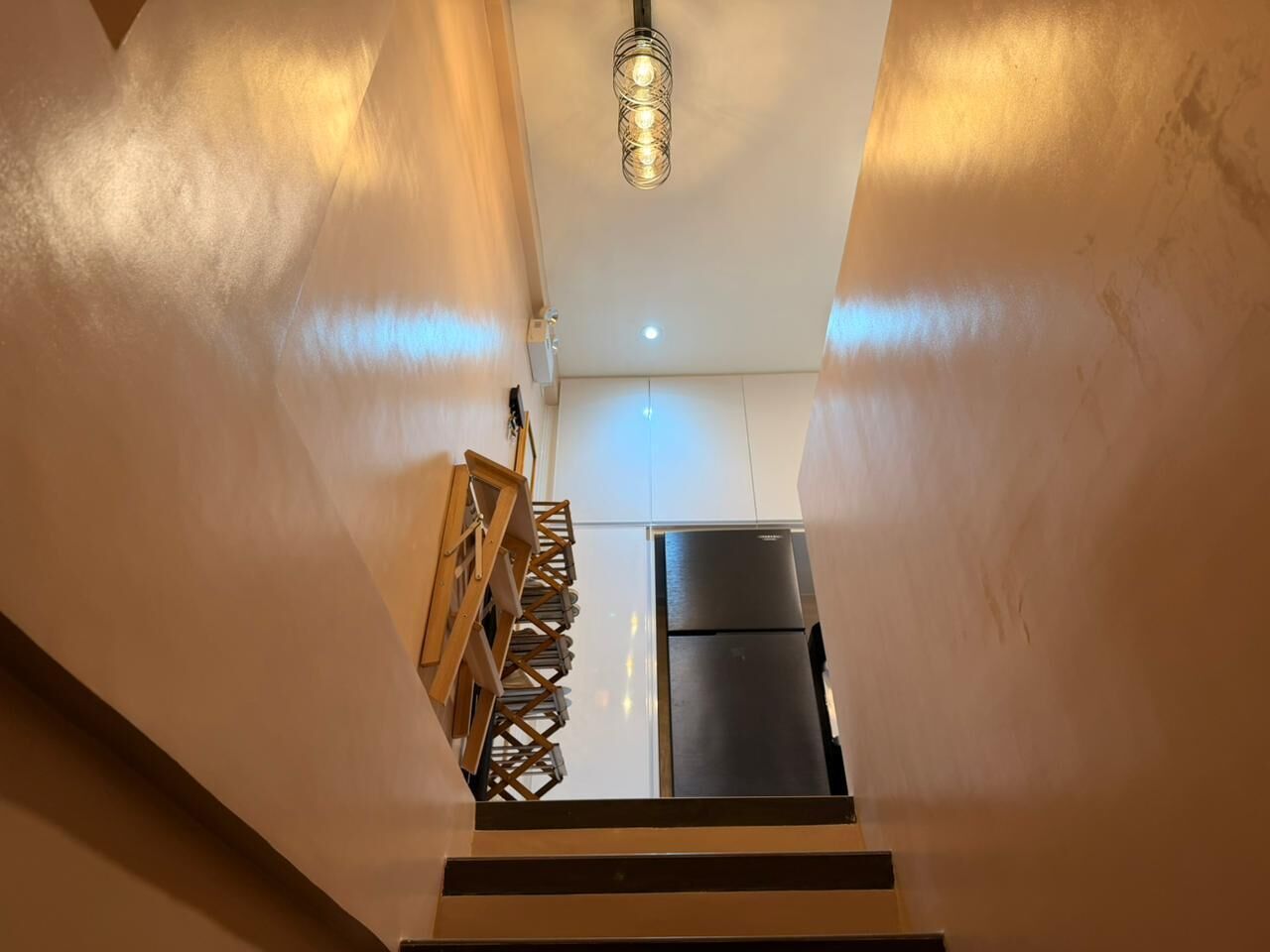A kitchen with a refrigerator and a hanging light fixture.