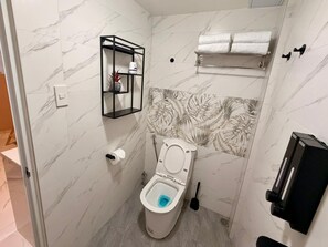Kylpyhuone, jossa on wc, hylly hygieniatuotteille, wc-paperiteline, pyyheteline ja käsienkuivaaja.