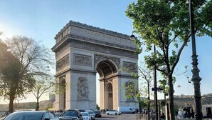 Uma rua de paralelepípedos que conduz a um grande arco histórico, com carros estacionados ao longo da lateral.