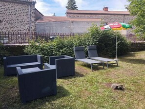 Terrasse mit Sitzgelegenheit, einem Steinmauerwerk und einem Ziegeldach im Hintergrund.