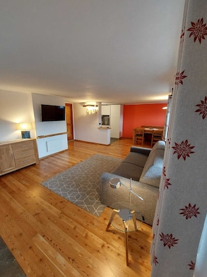 Ein Wohnzimmer mit einer Couch, einem Couchtisch, einem Fernseher und einer Küche im Hintergrund.