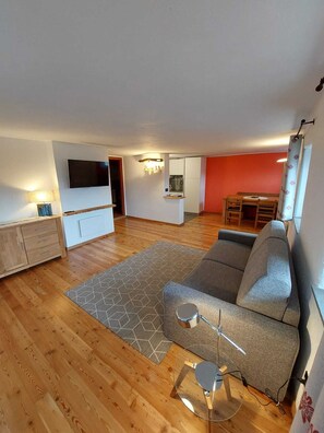 Ein Wohnzimmer mit Sofa, Fernseher, Esstisch und Küchenzeile.