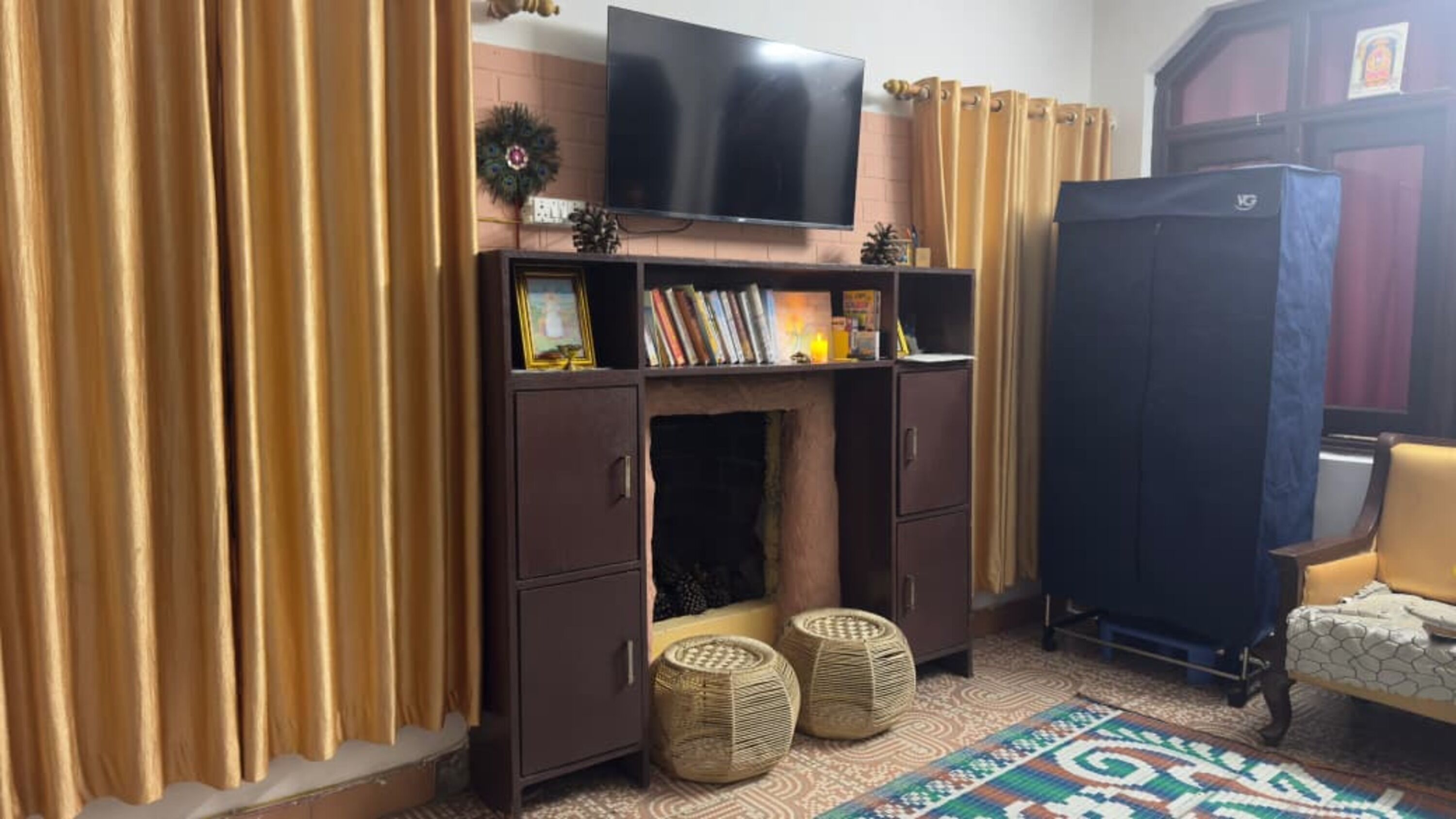 A living room with a television, books, a fireplace, wicker baskets, and a patterned rug.