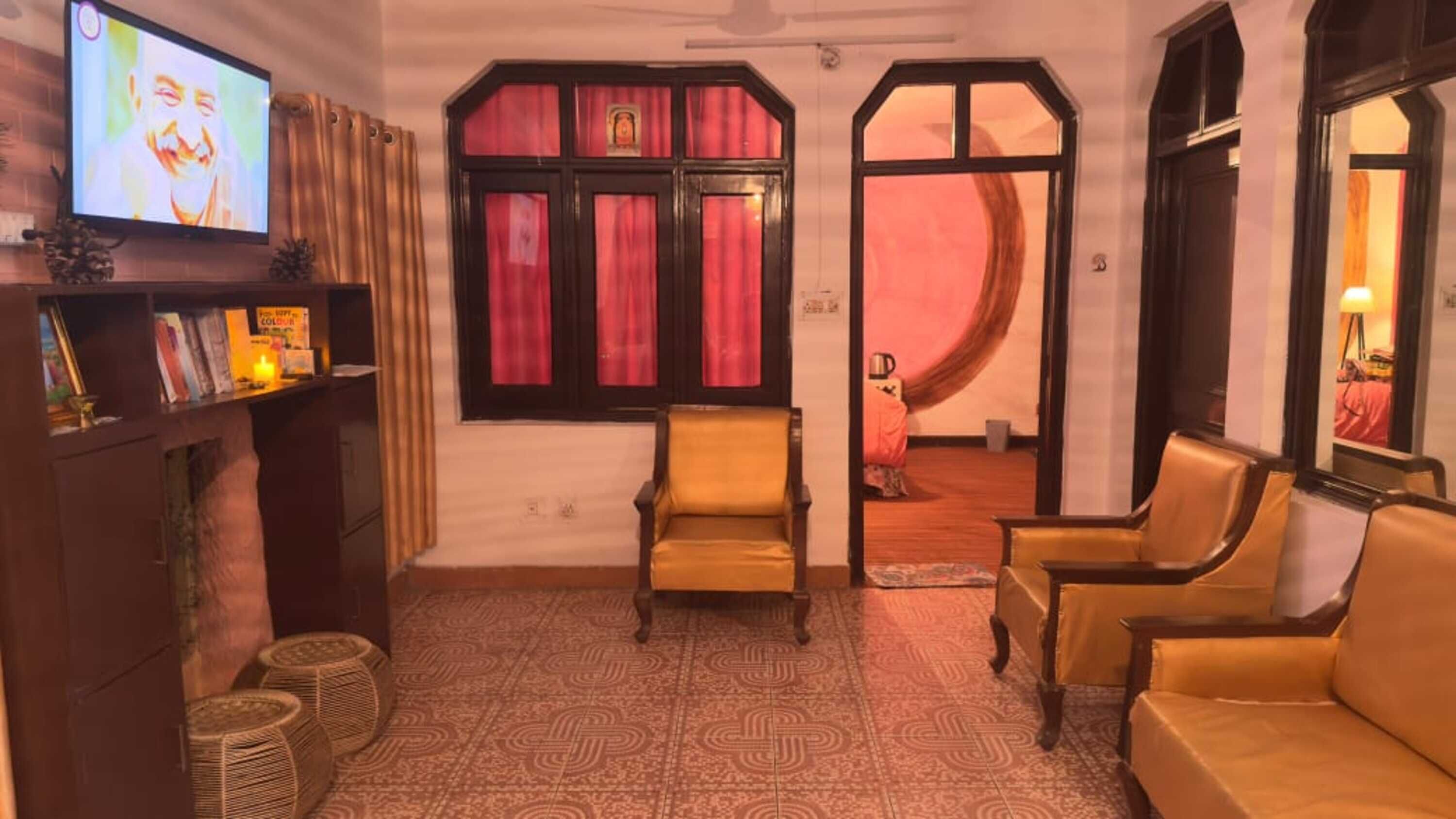 Une pièce avec une télévision, un canapé, un fauteuil, un sol à motifs et une fenêtre avec des rideaux rouges.