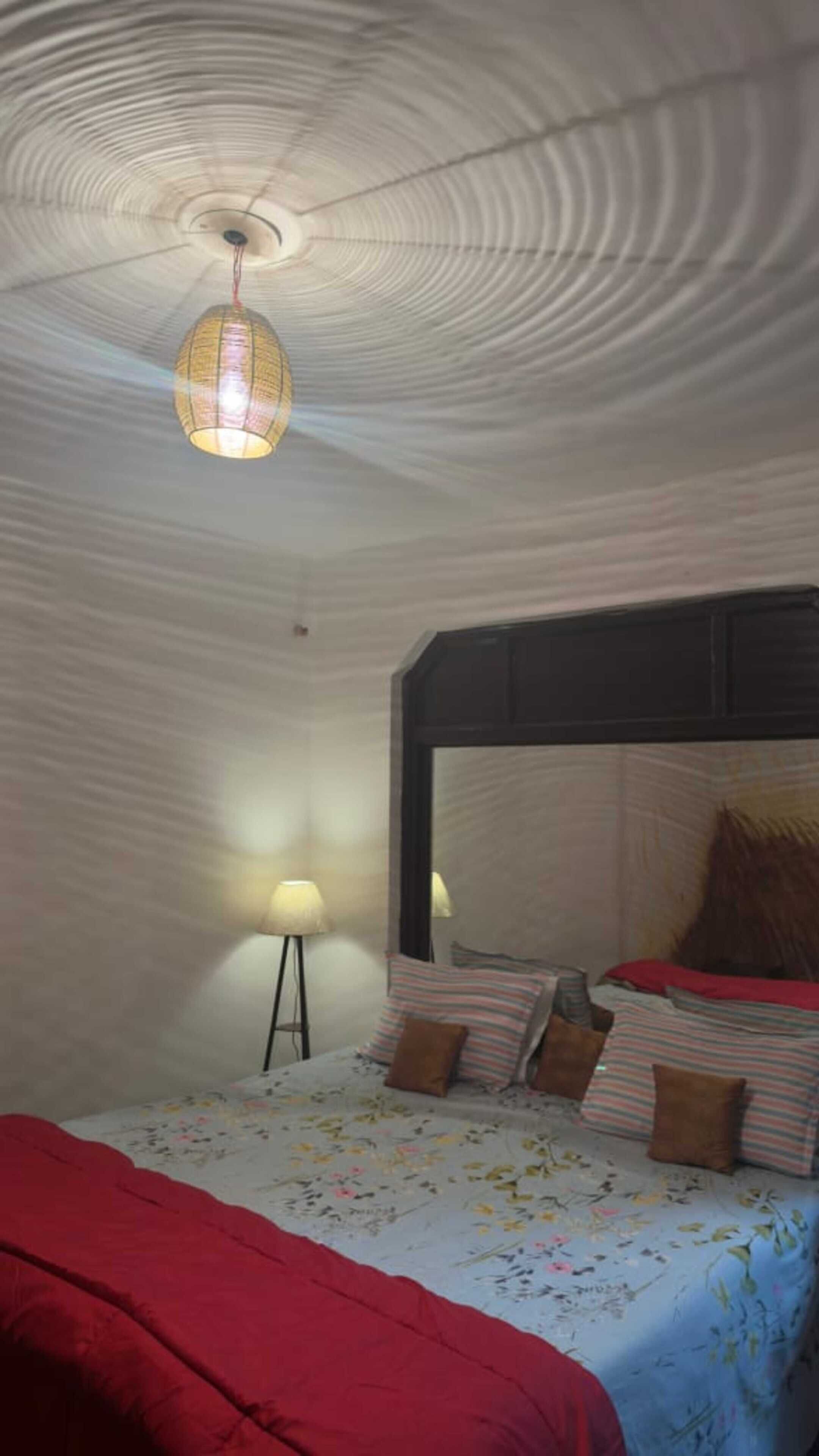 Quarto com cama, almofadas, abajur e um design de teto singular.
