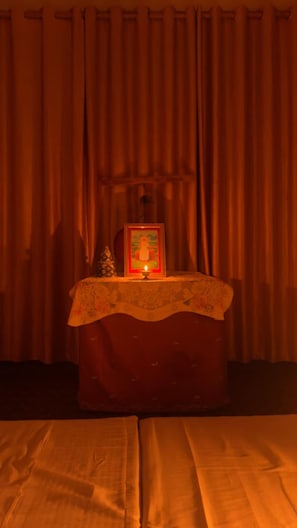 Una habitación con cama, una mesita con un cuadro enmarco y una vela, y cortinas.