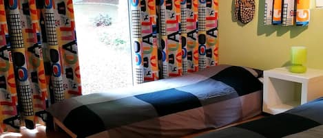 Quarto com cama, mesa de cabeceira e cortinas com padrão de paisagem urbana.
