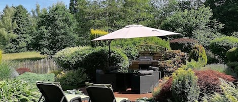 Un espace extérieur aménagé avec un barbecue, des chaises longues et un grand parasol.
