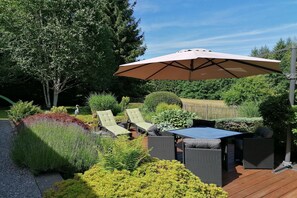 An outdoor patio with wicker furniture, a table, and a large umbrella. - Les Rainettes – Quiet family home with garden and terrace in the Ardennes (Grand-Halleux)