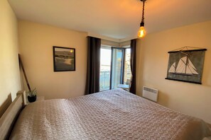 A hotel room with a bed, a window with curtains, a wall-mounted picture, and a hanging light fixture. - Sunny-side apartment in Nieuwpoort (NIEUWPOORT)