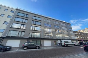 A multi-story building with balconies, a parking area, and a van parked in front. - Coastal Retreat in Nieuwpoort-Bad (NIEUWPOORT)