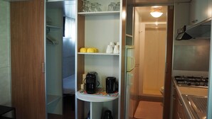 Una piccola cucina componibile con fornelli, macchina del caffè e scaffali con stoviglie.