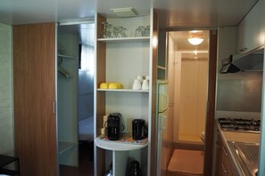 A compact kitchenette with a stove, coffee maker, and shelves with kitchenware. - Mobile Home with Private Veranda in Tuscany (Capannole)