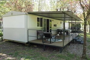 A mobile home with a covered porch, outdoor seating, and a small table. - Tuscan Mobile home with Covered Porch (Capannole)