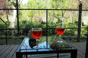 A table with two wine glasses and a bottle, set against a backdrop of greenery and trees. - Tuscan Mobile home with Covered Porch (Capannole)