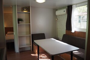A compact room with a bed, a table, a bench, a shelf with a clock, and a window with curtains. - Tuscan Mobile home with Covered Porch (Capannole)